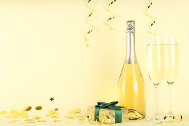 Photo of Shiny confetti, streamers, sparkling wine and gift box on beige background. Space for text