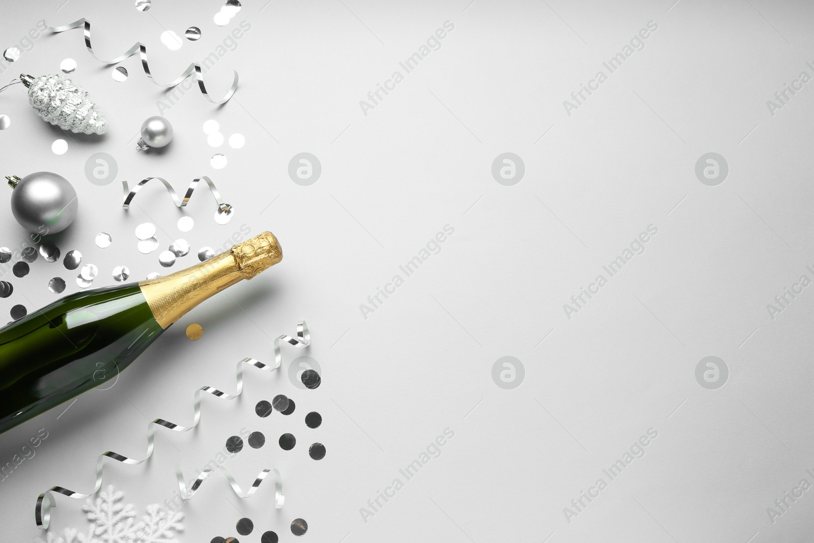 Photo of Flat lay composition with bottle of sparkling wine, shiny confetti and other Christmas decor on light grey background. Space for text