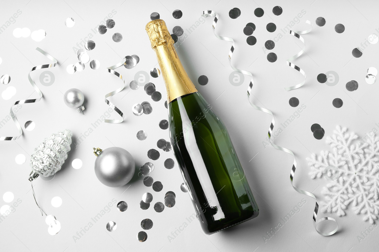 Photo of Flat lay composition with bottle of sparkling wine, shiny confetti and other Christmas decor on light grey background