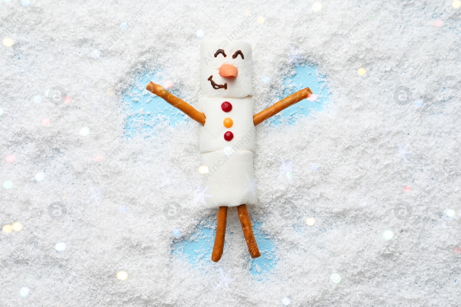 Photo of Marshmallow snowman making angel on artificial snow, top view