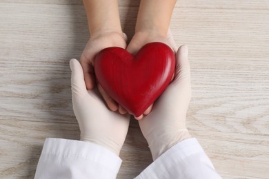 Photo of Doctor and child with heart model at white wooden table, top view