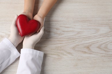 Photo of Doctor and child with heart model at white wooden table, top view. Space for text