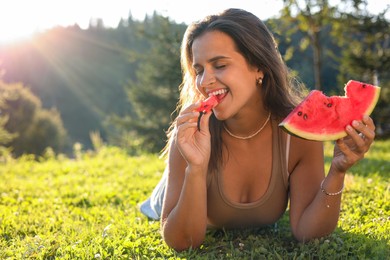 Happy woman eating juicy watermelon on green grass outdoors, space for text