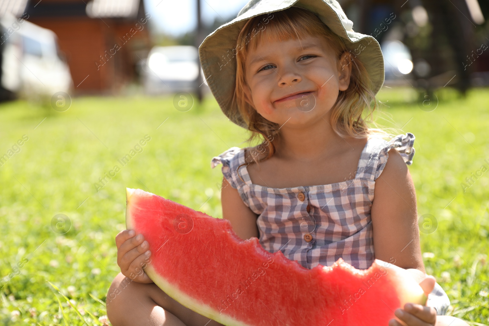 Photo of Cute little girl with slice of juicy watermelon on green grass outdoors