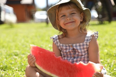 Photo of Cute little girl with slice of juicy watermelon on green grass outdoors