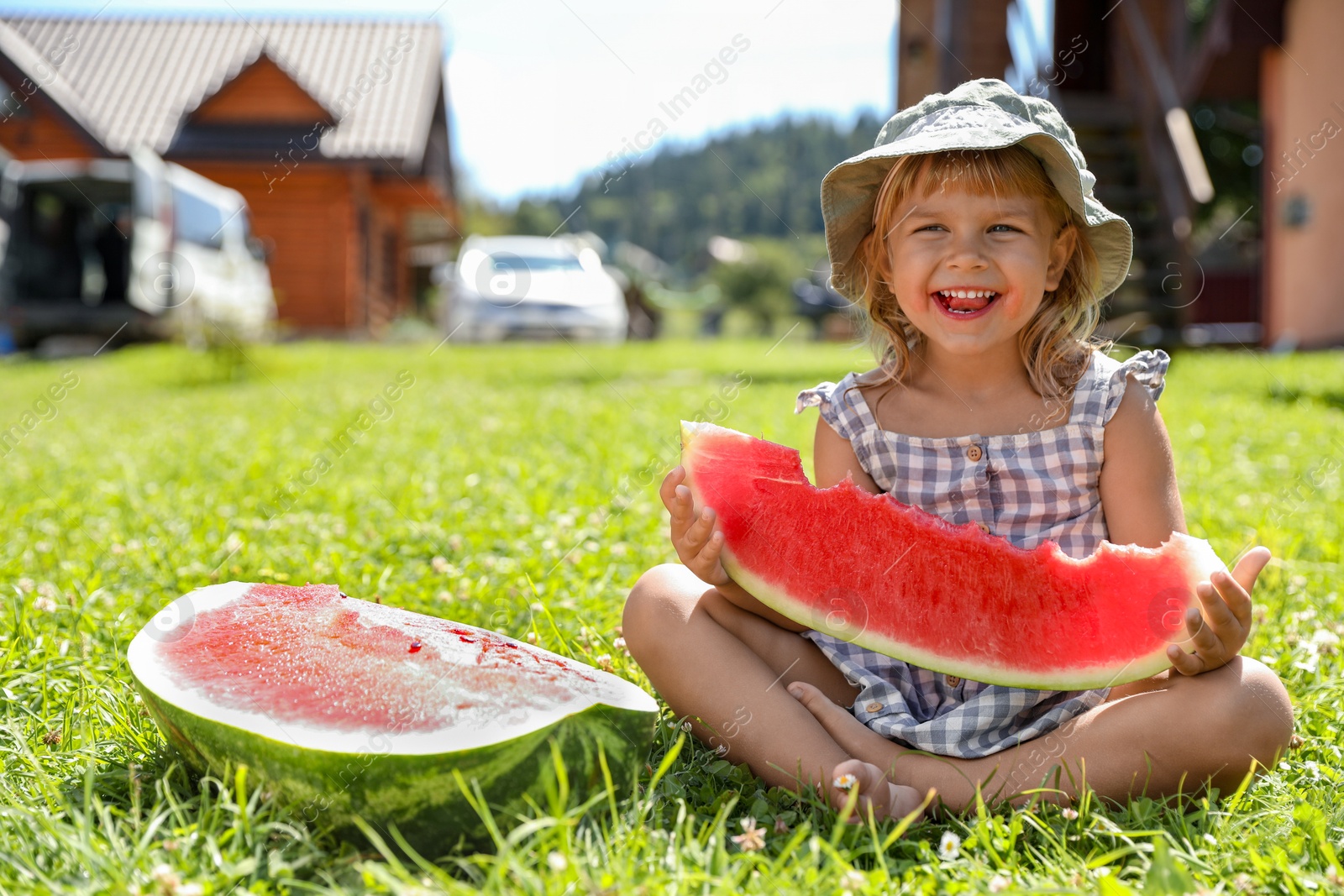 Photo of Cute little girl with slice of juicy watermelon on green grass outdoors