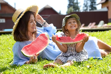 Mother and her daughter with slices of juicy watermelon on green grass outdoors