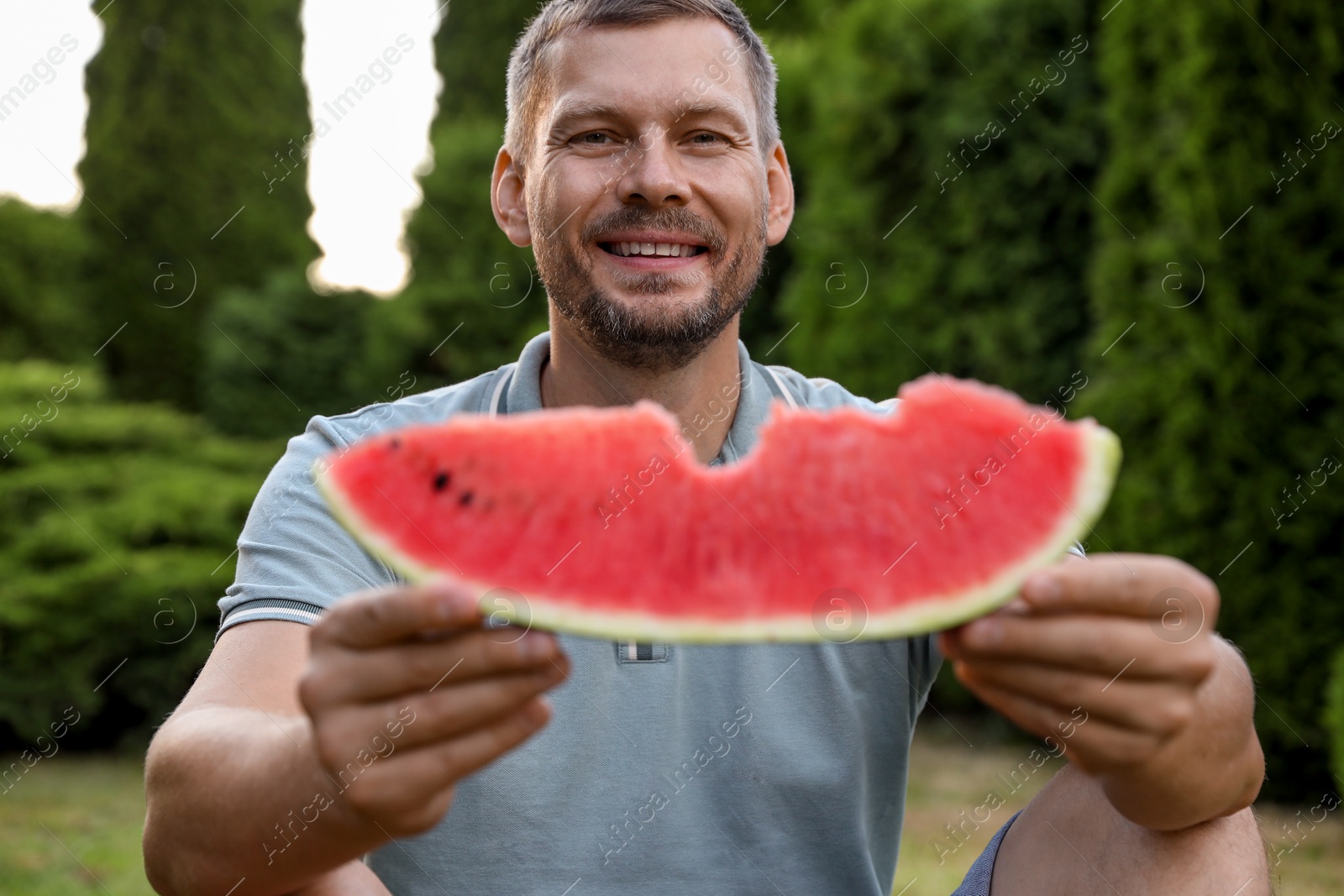 Photo of Happy man with slice of juicy watermelon outdoors