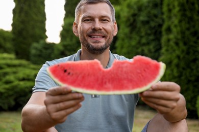 Happy man with slice of juicy watermelon outdoors