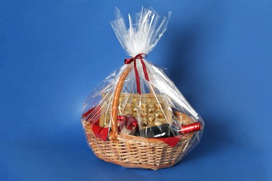 Photo of Wicker gift basket with wine on blue background