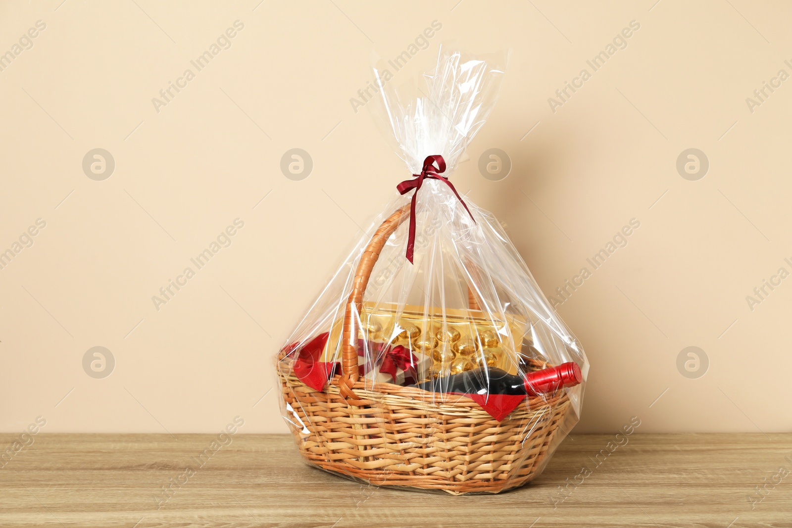 Photo of Wicker gift basket on wooden table against beige background