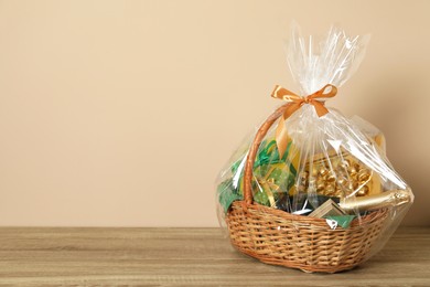 Photo of Wicker gift basket on wooden table against beige background. Space for text