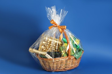 Photo of Wicker gift basket with wine on blue background