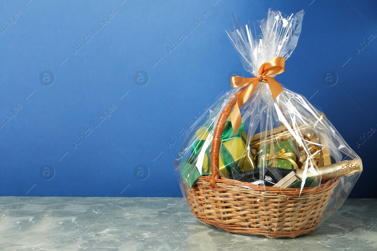 Photo of Wicker gift basket with wine on grey table against blue background. Space for text