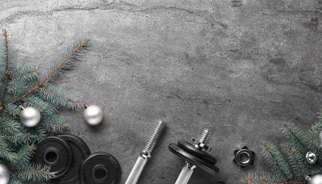 Photo of Barbell, dumbbell parts and Christmas decor on grey background, flat lay. Space for text