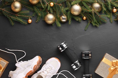 Photo of Dumbbells, gift box, sneakers and Christmas decor on black background, flat lay