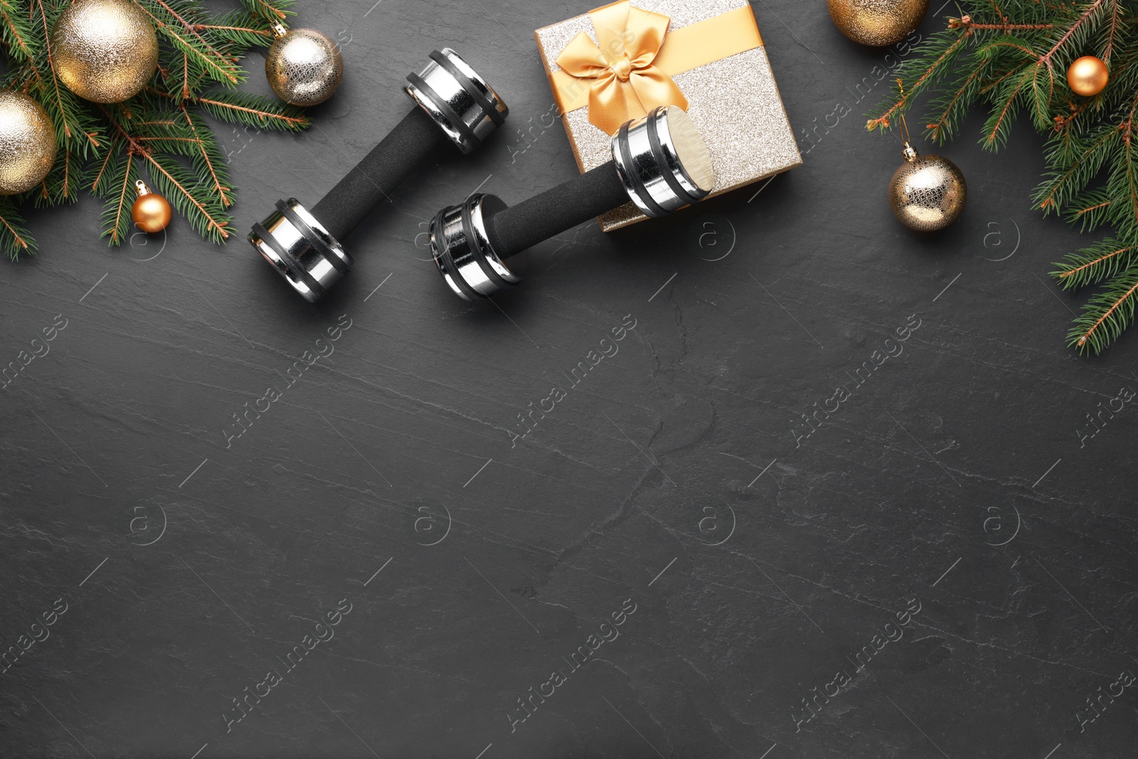 Photo of Dumbbells, gift box and Christmas decor on black background, flat lay. Space for text