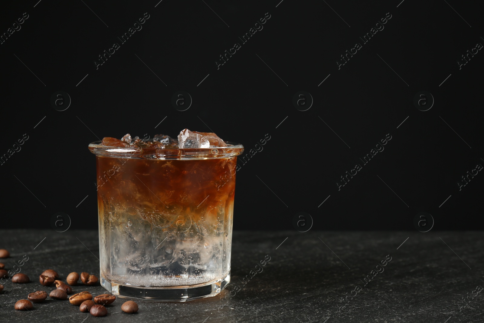 Photo of Refreshing espresso tonic drink and coffee beans on dark table. Space for text