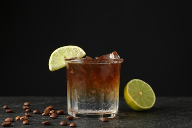 Photo of Refreshing espresso tonic drink with slice of lime and coffee beans on dark table