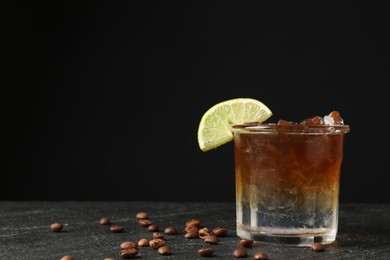 Photo of Refreshing espresso tonic drink with slice of lime and coffee beans on dark table. Space for text