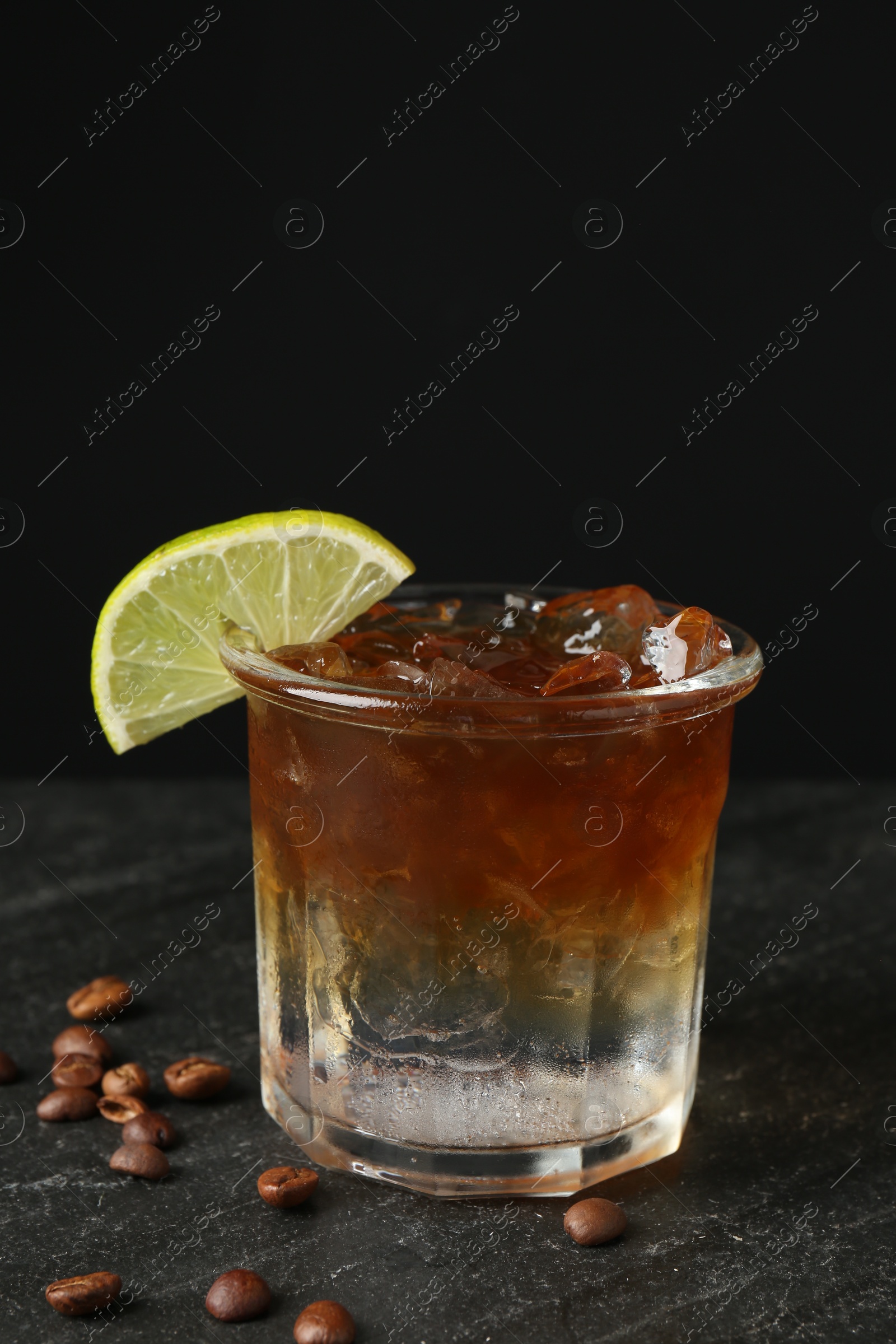 Photo of Refreshing espresso tonic drink with slice of lime and coffee beans on dark table