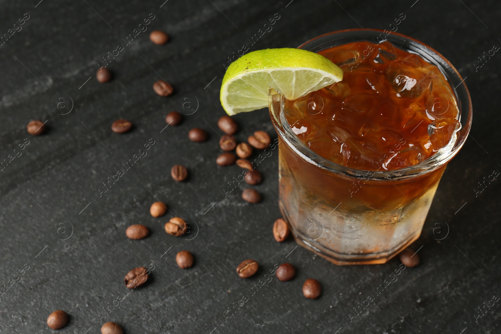 Photo of Refreshing espresso tonic drink with slice of lime and coffee beans on dark table, closeup