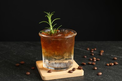 Refreshing espresso tonic drink with rosemary and coffee beans on dark table