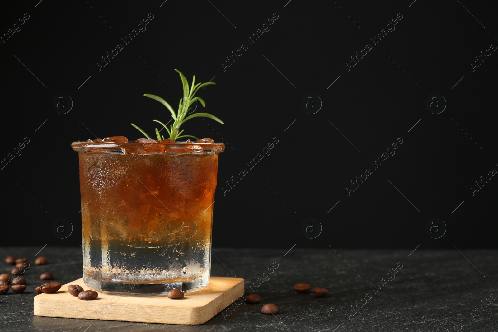 Photo of Refreshing espresso tonic drink with rosemary and coffee beans on dark table. Space for text