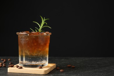 Refreshing espresso tonic drink with rosemary and coffee beans on dark table. Space for text