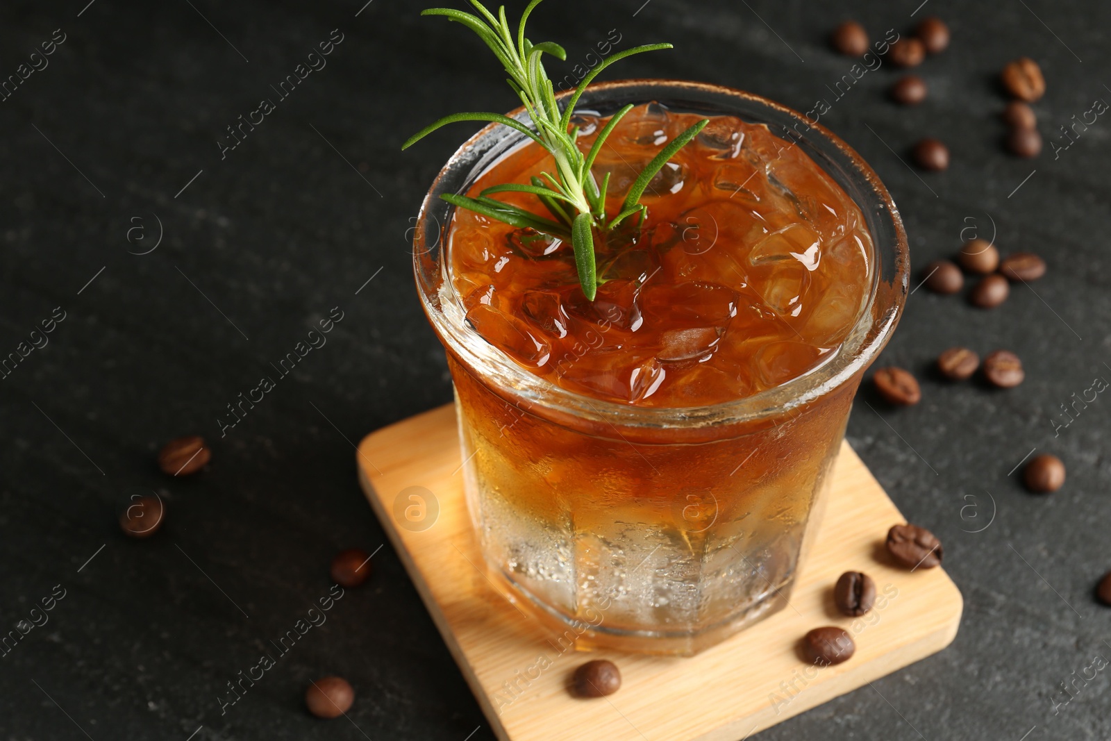 Photo of Refreshing espresso tonic drink with rosemary and coffee beans on dark table, closeup