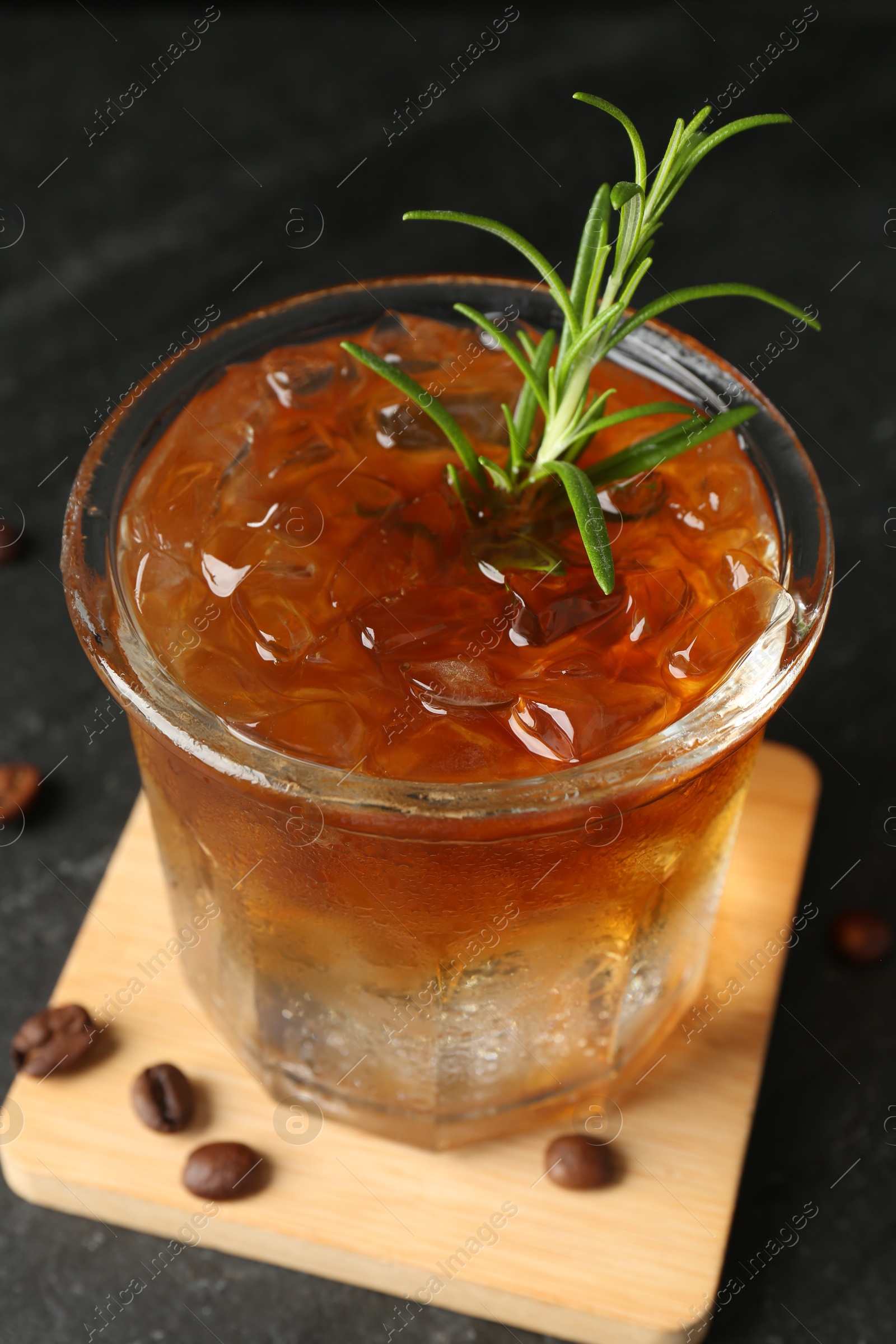 Photo of Refreshing espresso tonic drink with rosemary and coffee beans on dark table, closeup