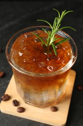 Refreshing espresso tonic drink with rosemary and coffee beans on dark table, closeup