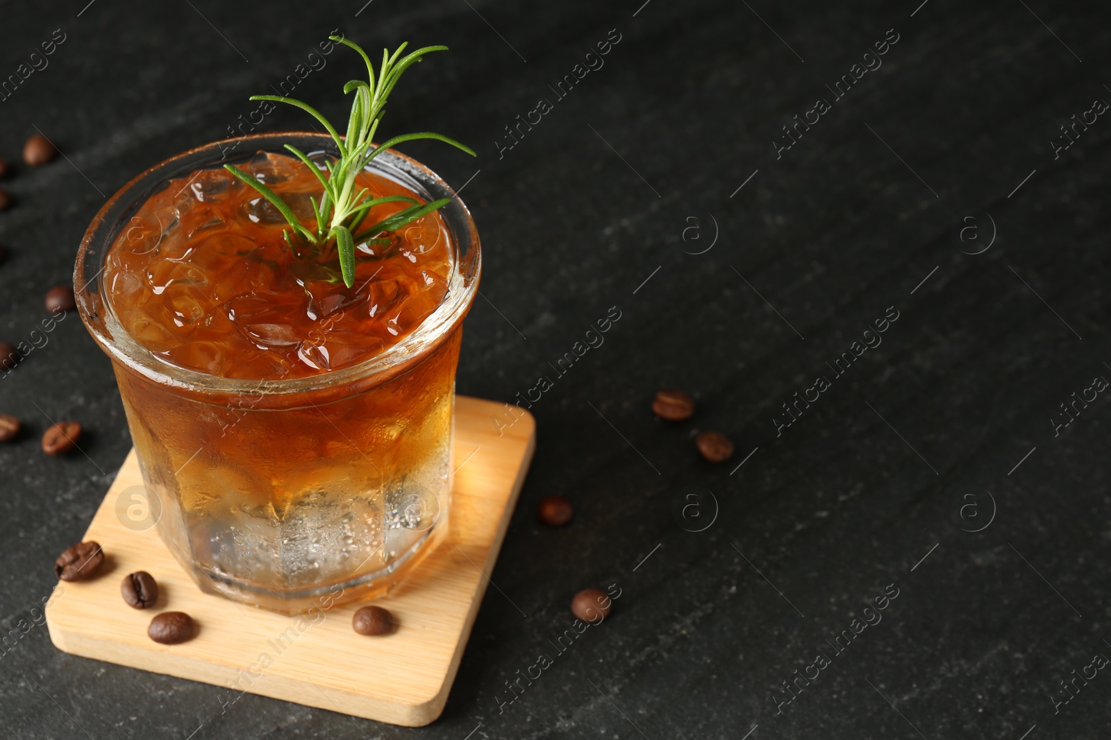 Photo of Refreshing espresso tonic drink with rosemary and coffee beans on dark table, closeup. Space for text