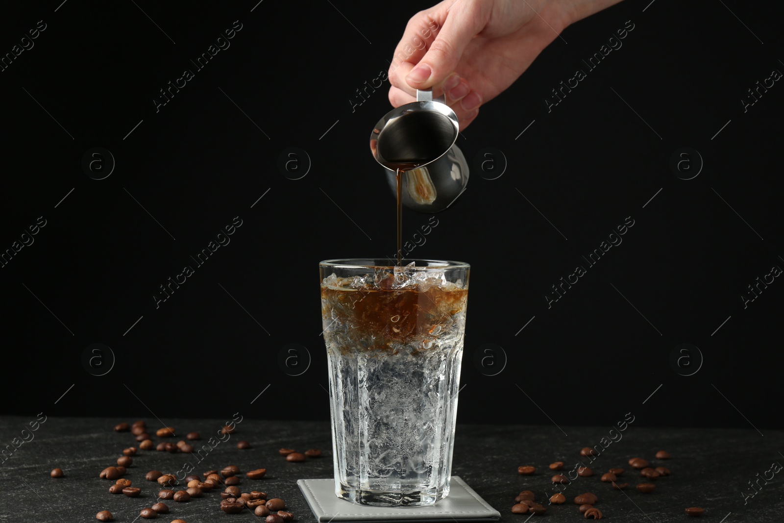 Photo of Woman making refreshing espresso tonic drink at dark table, closeup