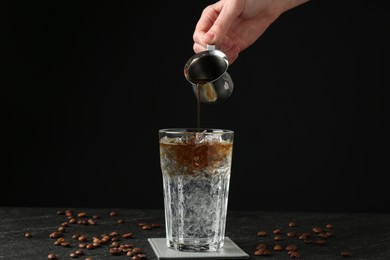 Photo of Woman making refreshing espresso tonic drink at dark table, closeup