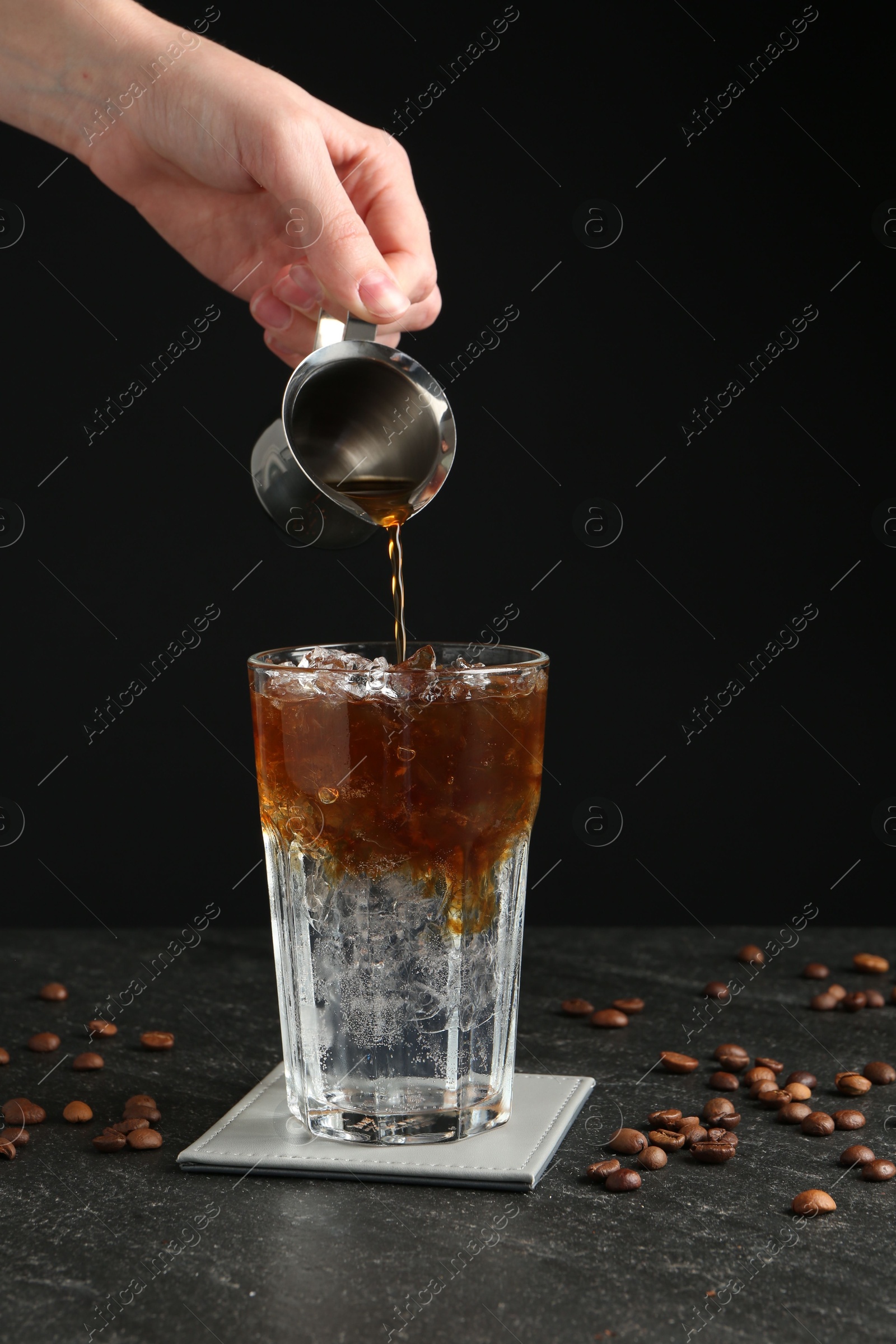 Photo of Woman making refreshing espresso tonic drink at dark table, closeup