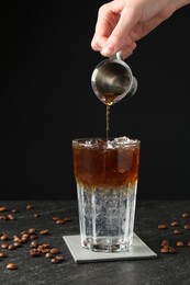 Photo of Woman making refreshing espresso tonic drink at dark table, closeup