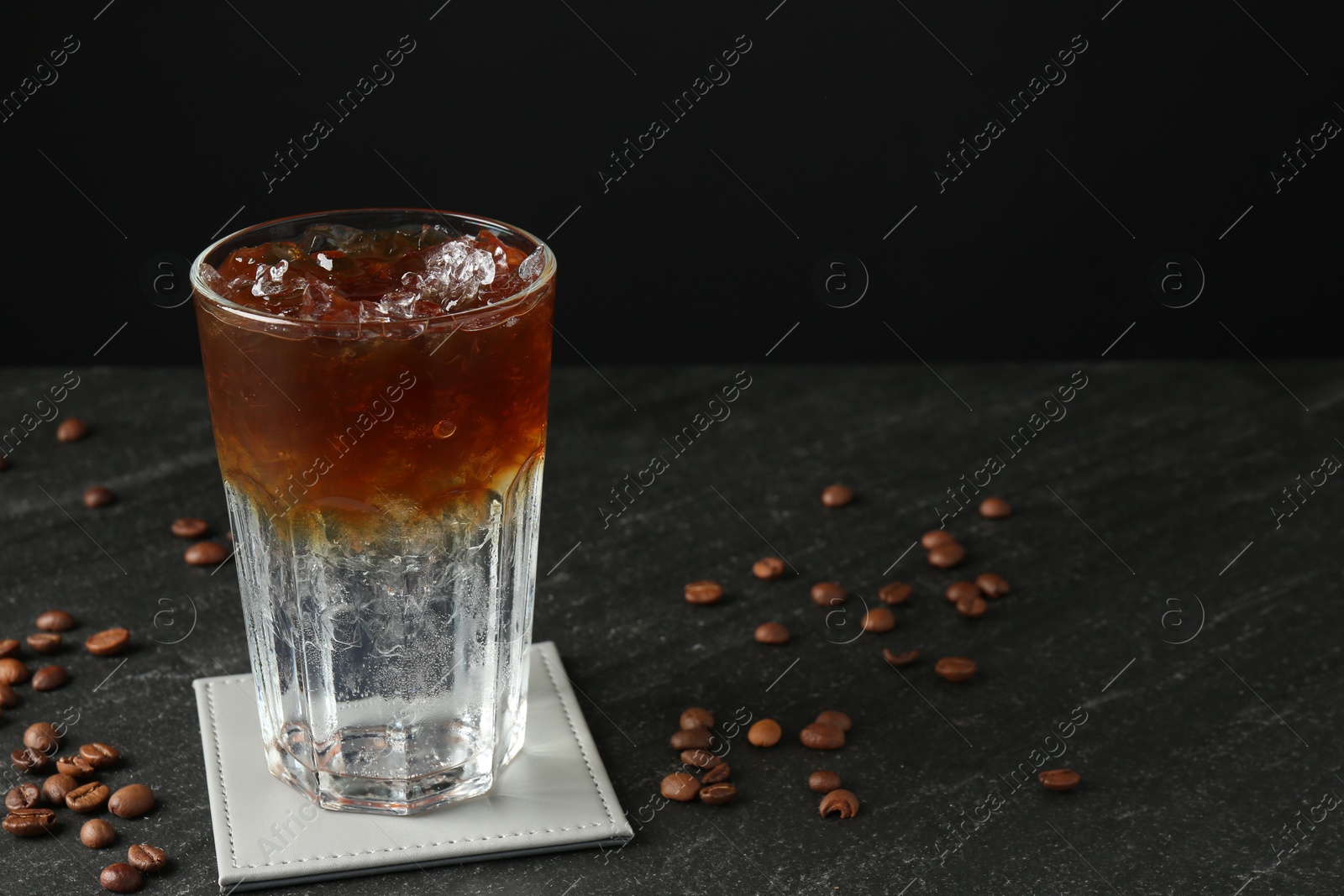 Photo of Refreshing espresso tonic drink and coffee beans on dark table. Space for text