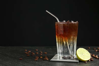 Photo of Refreshing espresso tonic drink with slice of lime and coffee beans on dark table. Space for text