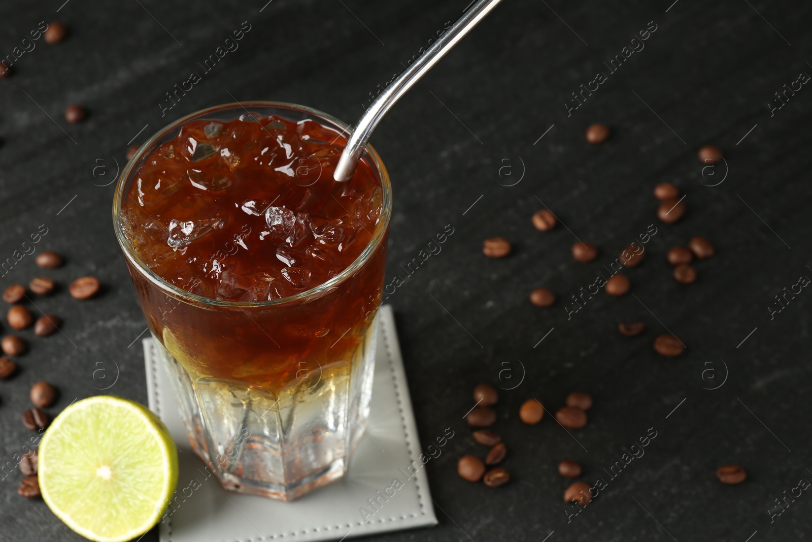 Photo of Refreshing espresso tonic drink with slice of lime and coffee beans on dark table, closeup