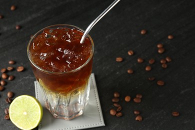 Refreshing espresso tonic drink with slice of lime and coffee beans on dark table, closeup