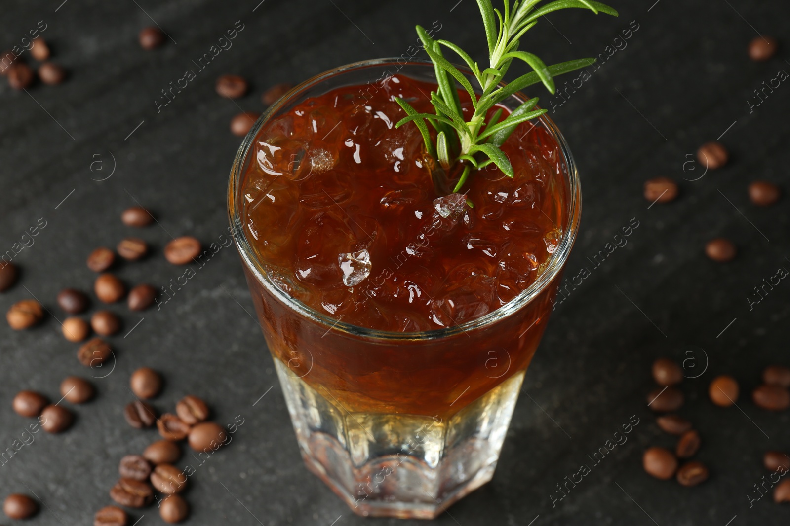 Photo of Refreshing espresso tonic drink with rosemary and coffee beans on dark table, closeup