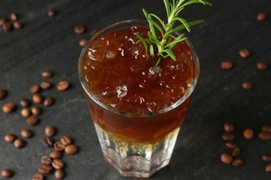 Refreshing espresso tonic drink with rosemary and coffee beans on dark table, closeup