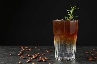 Refreshing espresso tonic drink with rosemary and coffee beans on dark table. Space for text