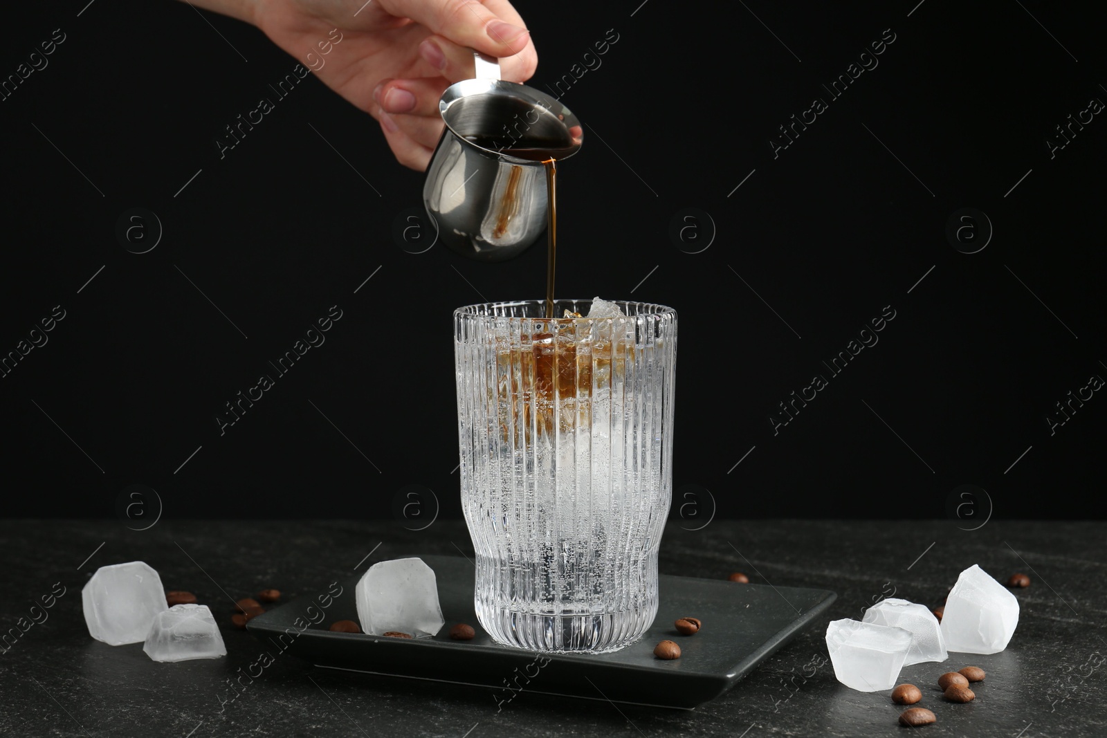 Photo of Woman making refreshing espresso tonic drink at dark table, closeup