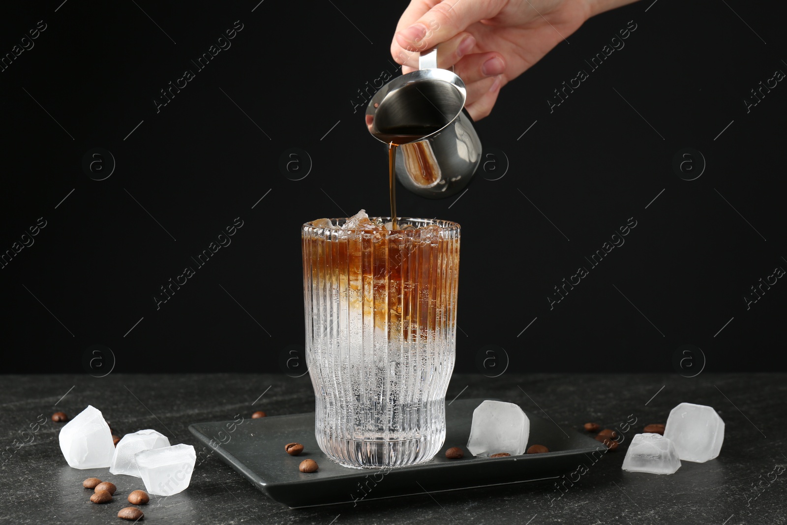 Photo of Woman making refreshing espresso tonic drink at dark table, closeup