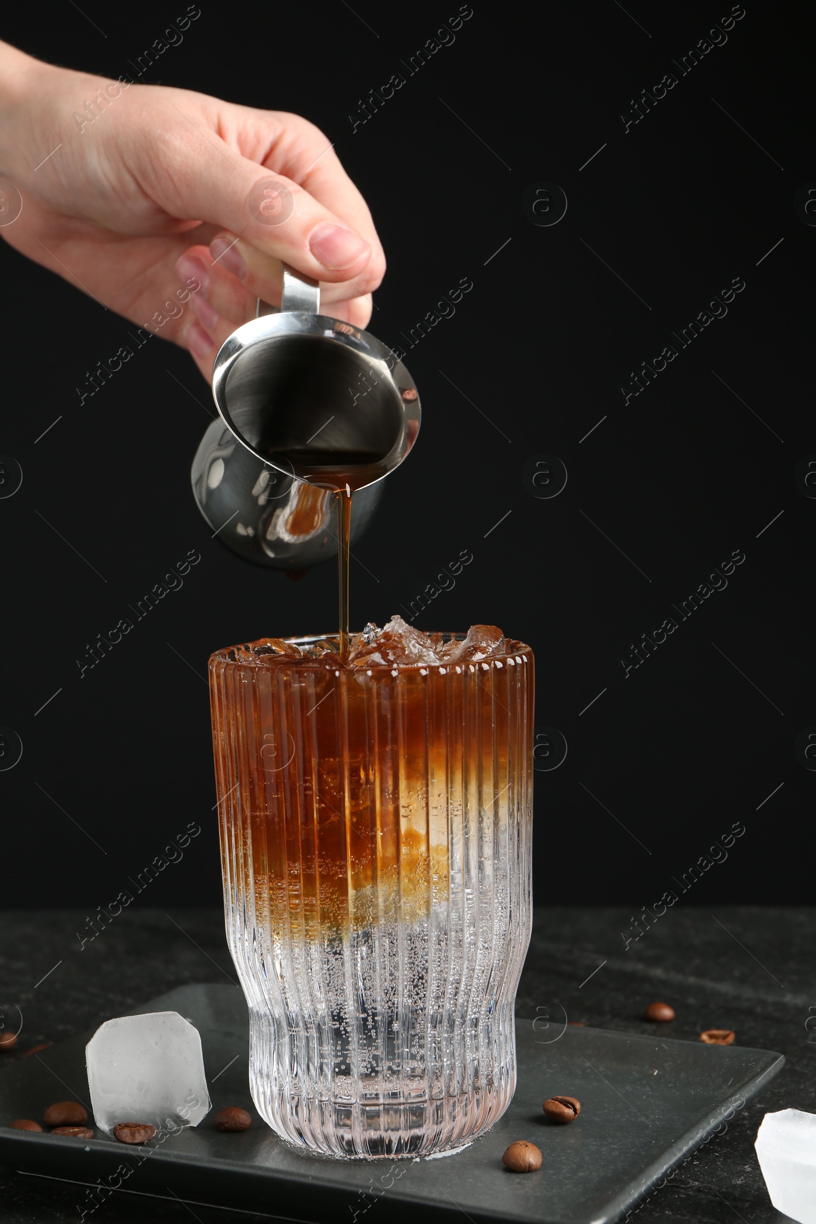 Photo of Woman making refreshing espresso tonic drink at dark table, closeup