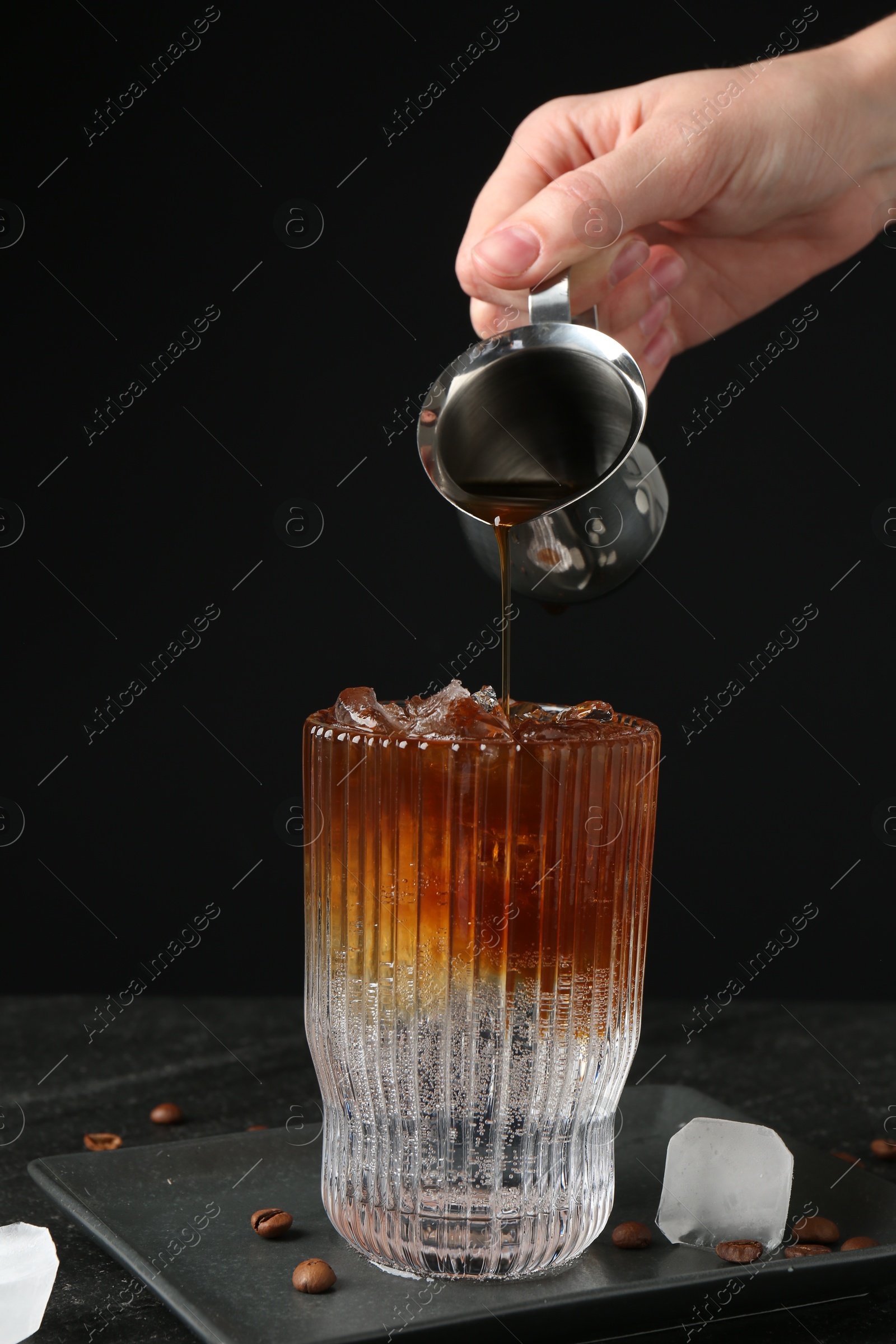 Photo of Woman making refreshing espresso tonic drink at dark table, closeup