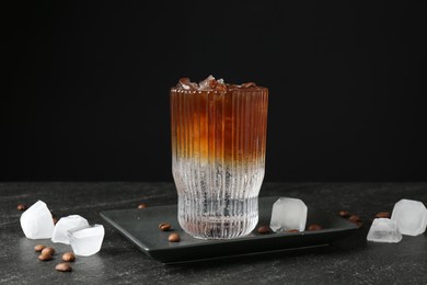 Photo of Refreshing espresso tonic drink with ice and coffee beans on dark table