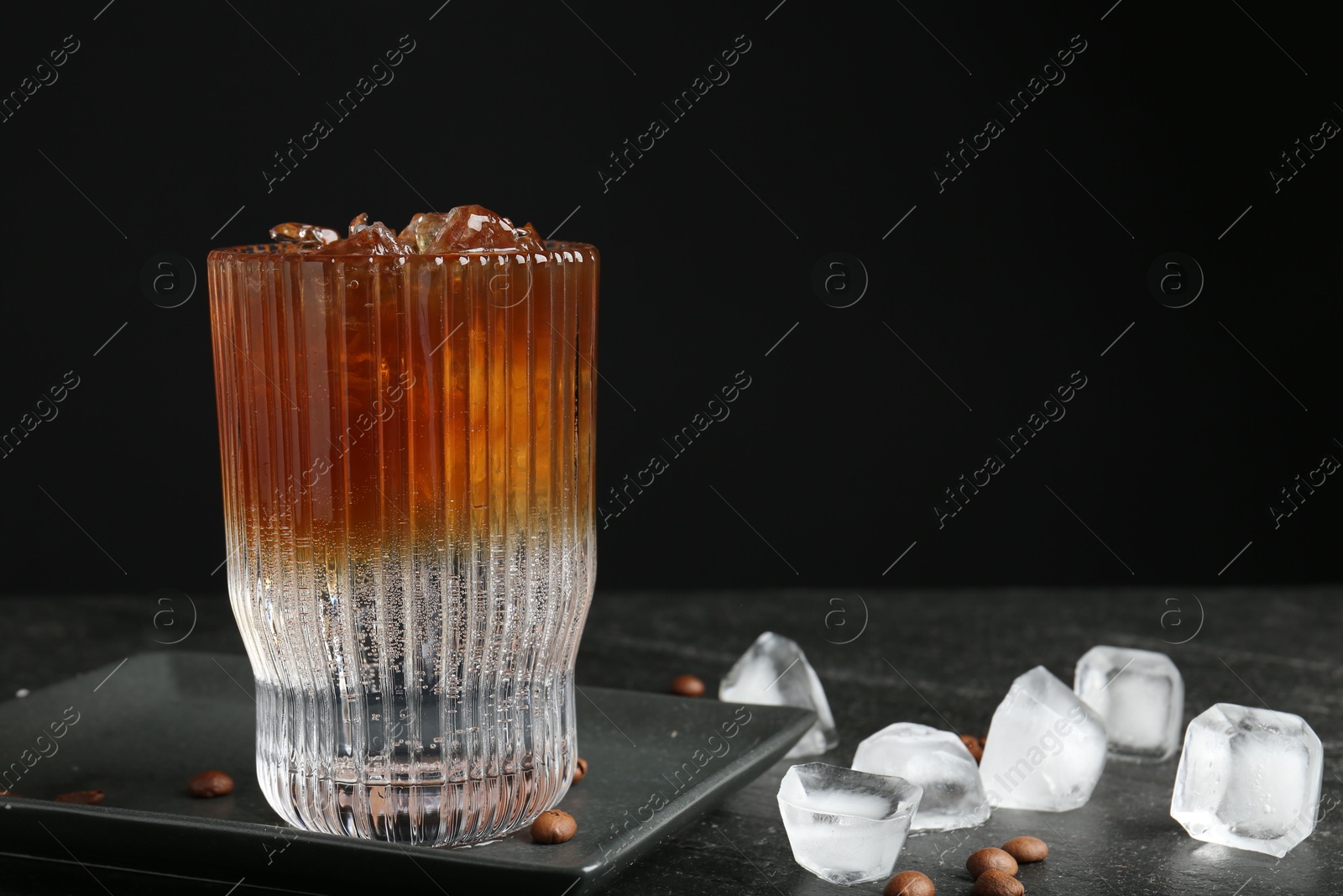 Photo of Refreshing espresso tonic drink with ice and coffee beans on dark table, closeup. Space for text